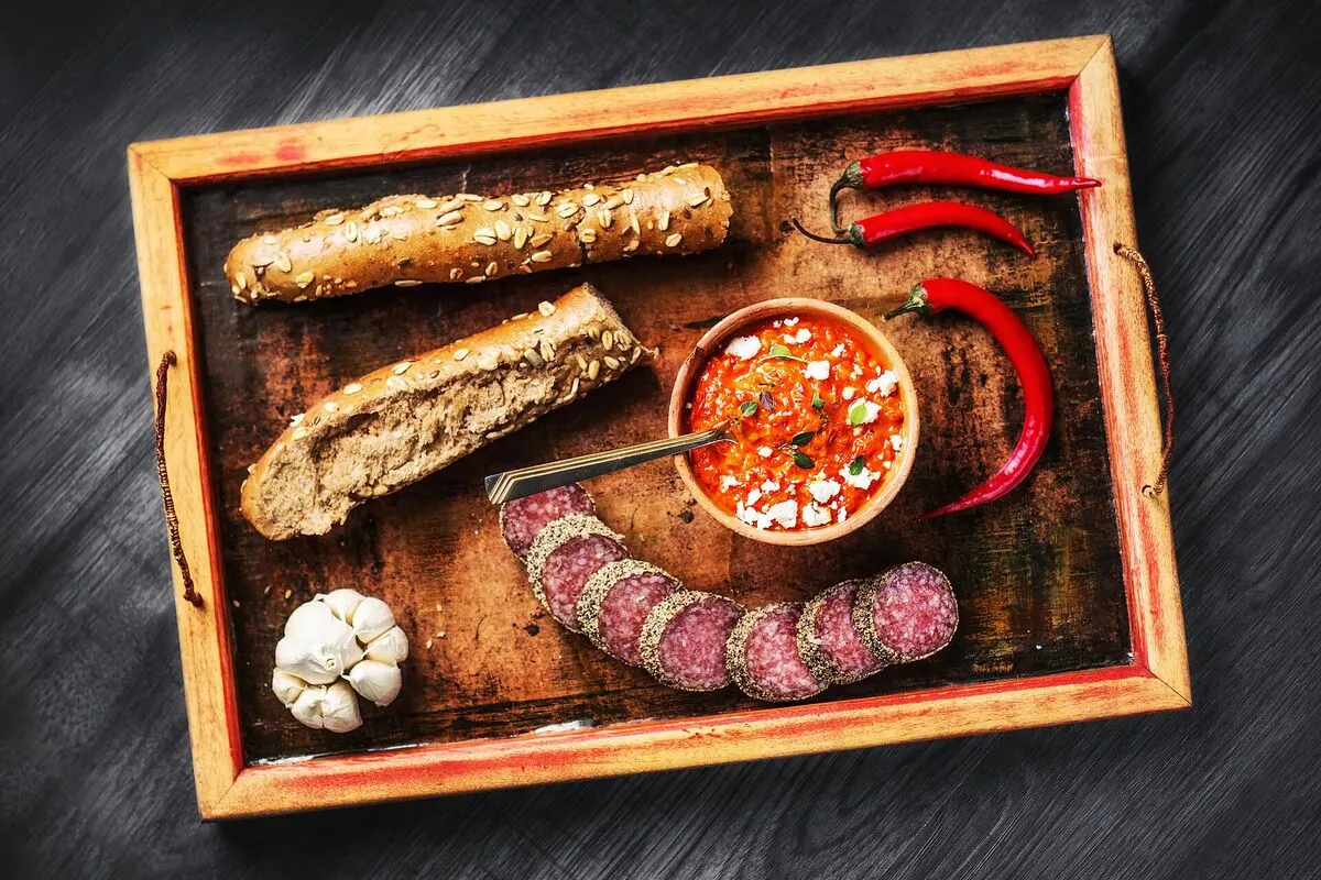 Drewniana taca z pieczywem, plastrami salami, papryczkami chili, czosnkiem i miseczką ajwaru