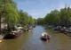 Amsterdamski kanał obsadzony drzewami, z zacumowanymi barkami i płynącą łodzią