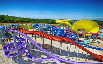 Kolorowe, kręte zjeżdżalnie wodne w aquaparku Aquacolors w Poreču na tle lasu i błękitnego nieba