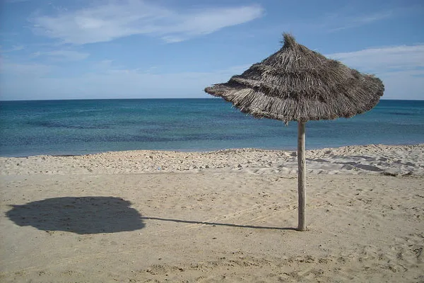 Piaszczysta plaża ze słomianym parasolem nad morzem