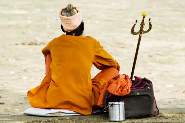 Sadhu w szafranowej szacie siedzący tyłem obok trójzębu i bagażu