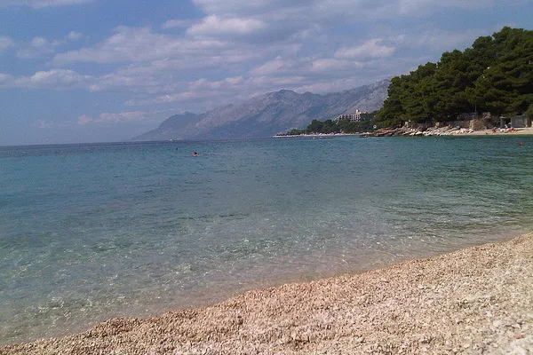 Jasna żwirowa plaża w Breli z przejrzystą wodą i masywem Biokovo w tle