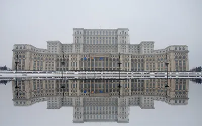 Monumentalna fasada Pałacu Parlamentu w Bukareszcie odbita w tafli wody zimą