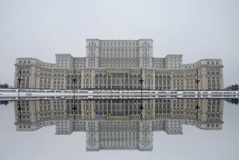 Monumentalna fasada Pałacu Parlamentu w Bukareszcie odbita w tafli wody zimą