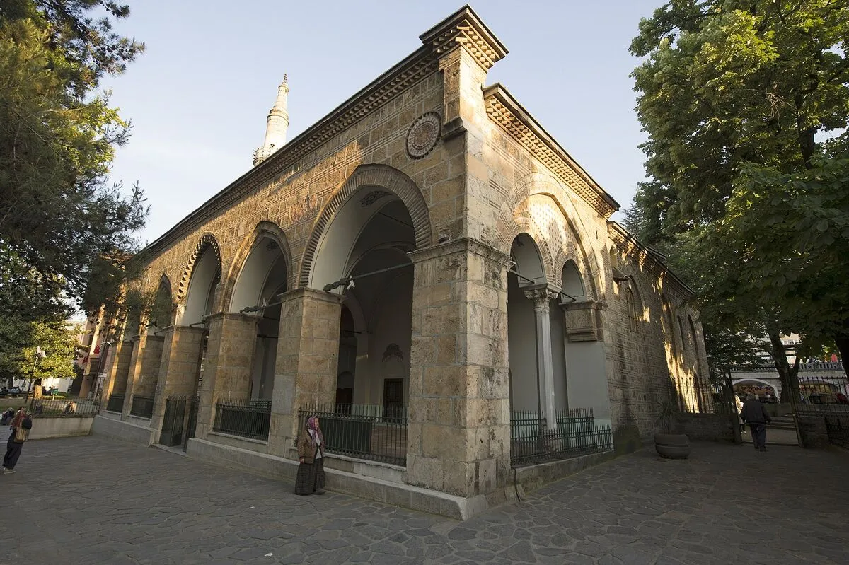 Kamienno-ceglana fasada meczetu Orhana Gazi w Bursie z łukowymi arkadami i smukłym minaretem
