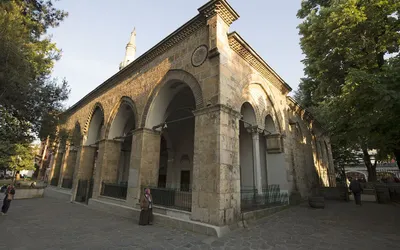 Kamienno-ceglana fasada meczetu Orhana Gazi w Bursie z łukowymi arkadami i smukłym minaretem