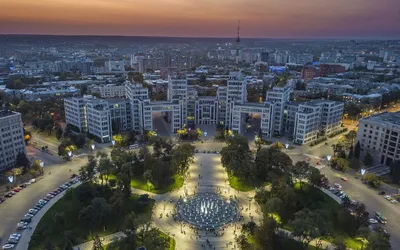 Plac Wolności w Charkowie z lotu ptaka o zmierzchu: oświetlona fontanna i aleja, w głębi konstruktywistyczny gmach Dzierżpromu