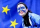 Uśmiechnięta dziewczyna z twarzą pomalowaną w barwy Unii Europejskiej na tle flagi UE