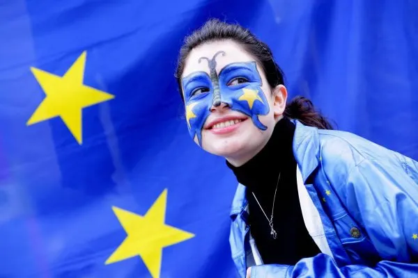 Uśmiechnięta dziewczyna z twarzą pomalowaną w barwy Unii Europejskiej na tle flagi UE