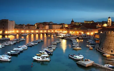 Stary port w Dubrowniku nocą, z oświetlonymi murami miasta