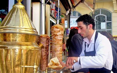 Sprzedawca ulicznego baru nakłada döner kebab z obrotowego rożna do chleba