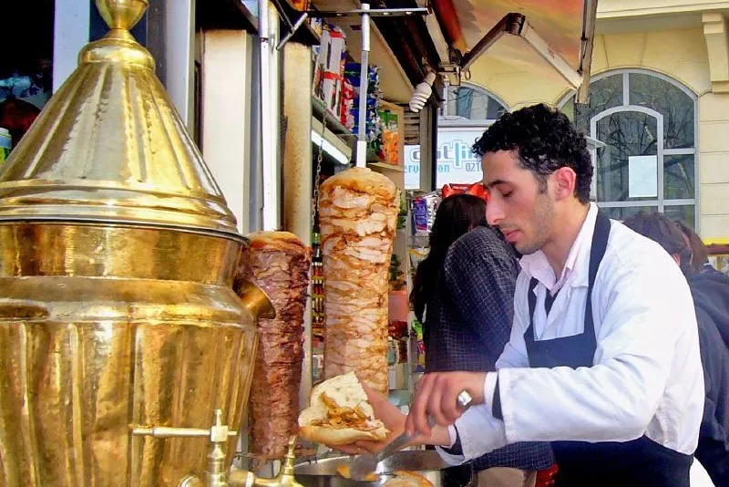 Sprzedawca ulicznego baru nakłada döner kebab z obrotowego rożna do chleba