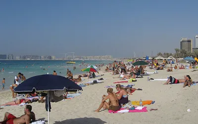 Turyści w strojach kąpielowych na zatłoczonej publicznej plaży w Dubaju