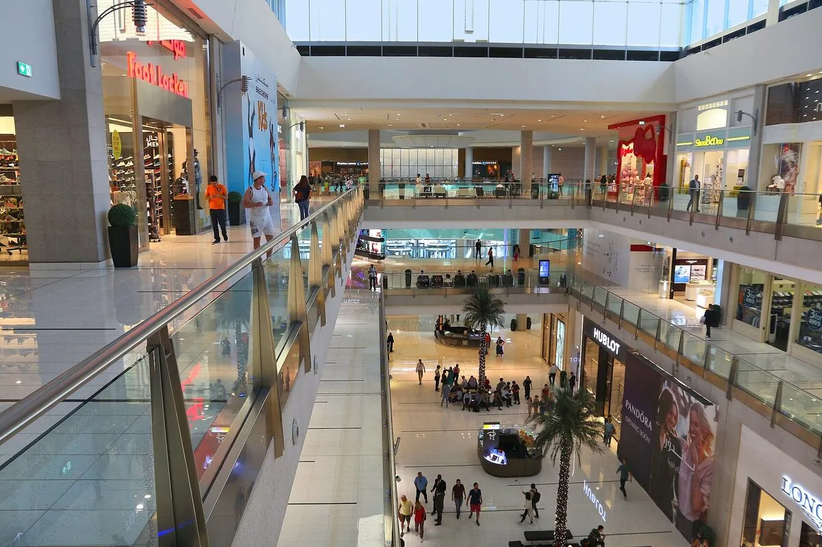 Wielopoziomowe wnętrze Dubai Mall z przeszklonymi balustradami, sklepami i palmami na parterze