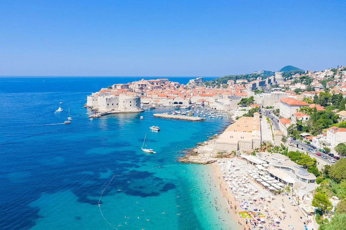 Plaża Banje z parasolami, a za nią Stare Miasto z fortecą i stary port w Dubrowniku, widok z góry