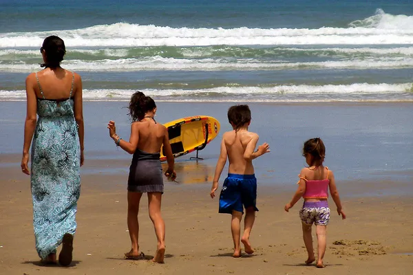 Kobieta i troje dzieci idą po piaszczystej plaży w stronę fal
