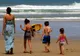 Kobieta i troje dzieci idą po piaszczystej plaży w stronę fal