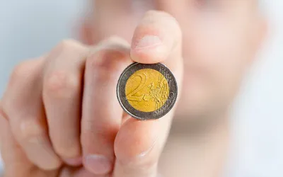 Moneta 2 euro trzymana w palcach na rozmytym tle