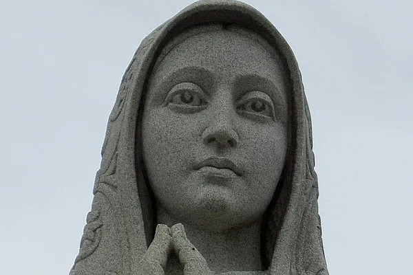 Kamienna figura Matki Bożej ze złożonymi do modlitwy dłońmi