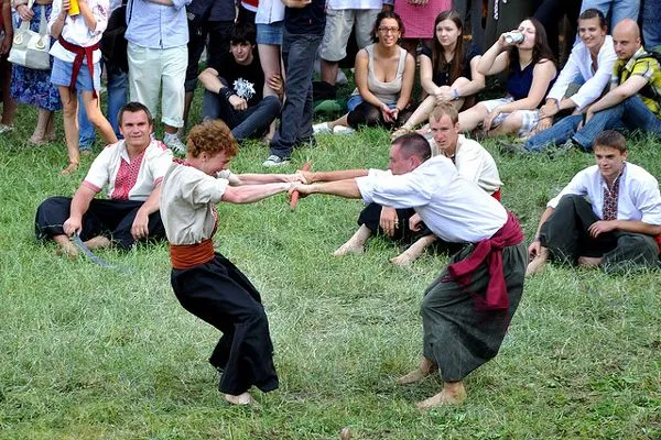 Mężczyźni w kozackich strojach mocują się na trawie przed publicznością festiwalu