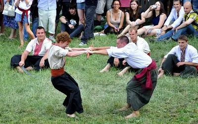Mężczyźni w kozackich strojach mocują się na trawie przed publicznością festiwalu