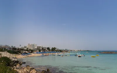 Piaszczysta plaża z parasolami w zatoce Fig Tree Bay w Protaras, w tle hotele i turkusowe morze z łodziami