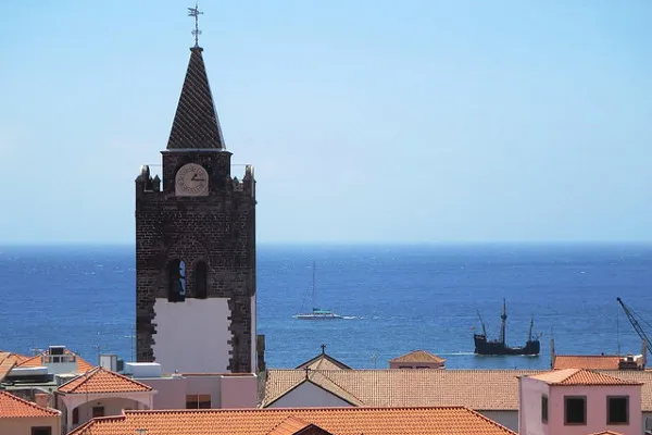 Dzwonnica i dachy Funchal, w tle ocean i replika żaglowca
