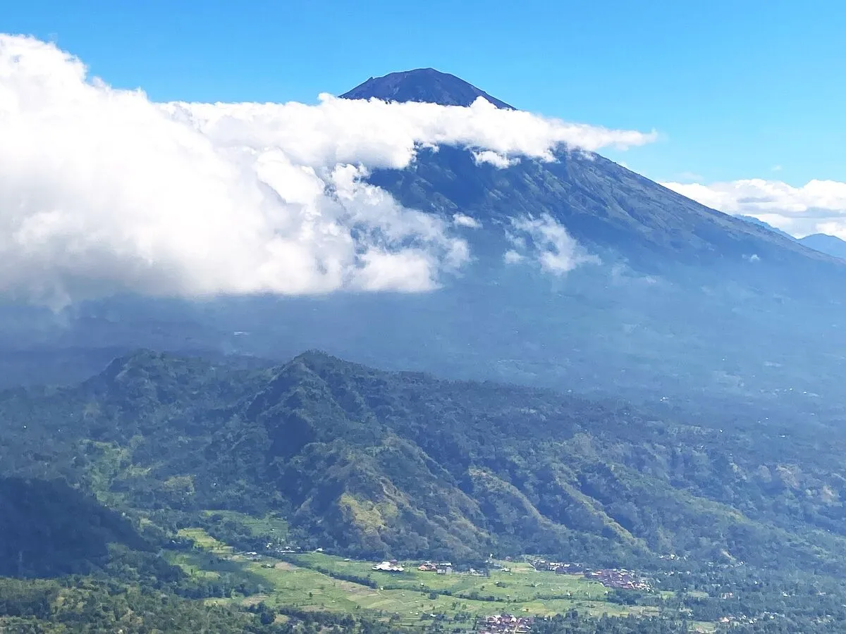 Stożek wulkanu Gunung Agung częściowo w chmurach, poniżej zielona dolina