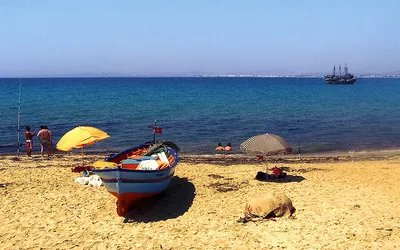 Kolorowa łódź rybacka i parasole na piaszczystej plaży w Hammamecie