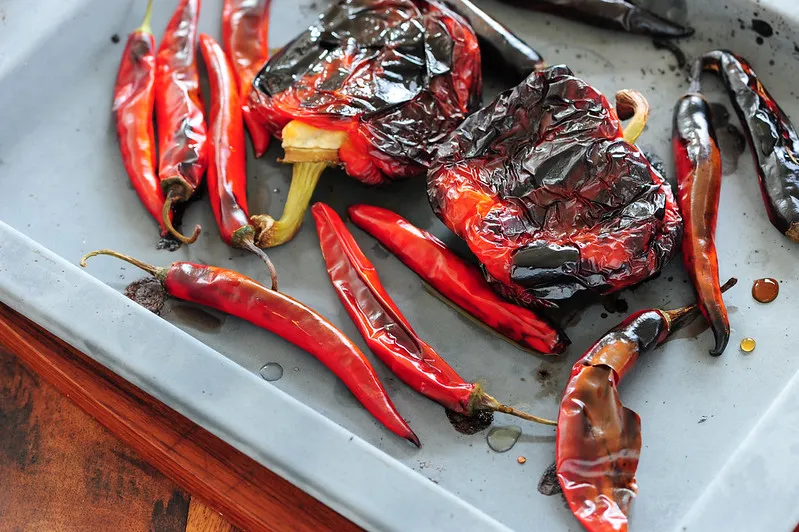 Upieczone czerwone papryki i papryczki chili na blasze, gotowe do przygotowania harissy