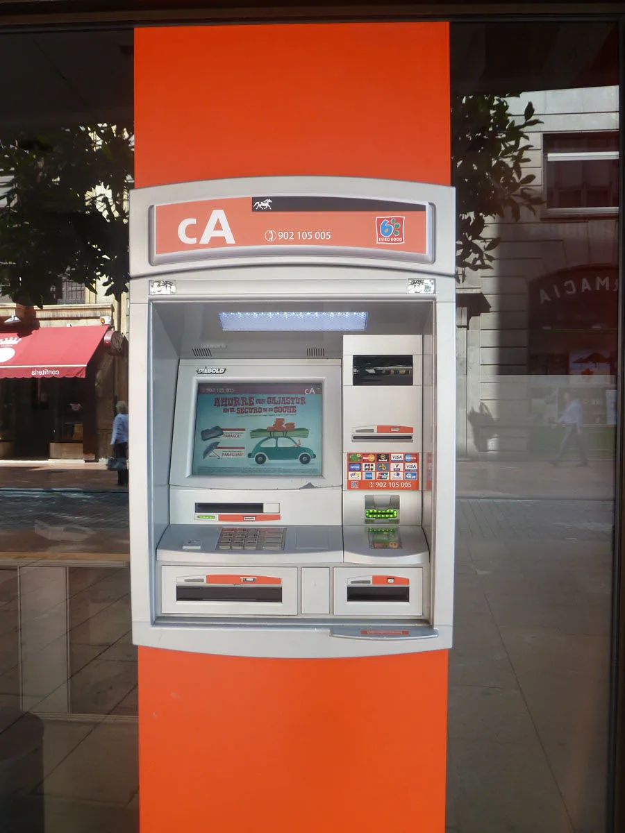 Bankomat w pomarańczowej obudowie w szklanej ścianie banku przy ulicy