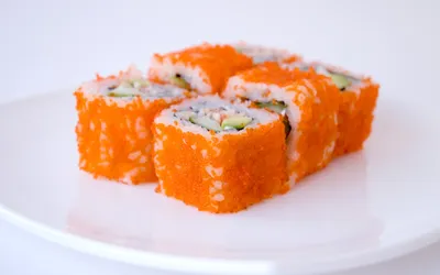 Roladki sushi obsypane pomarańczową ikrą na białym talerzu