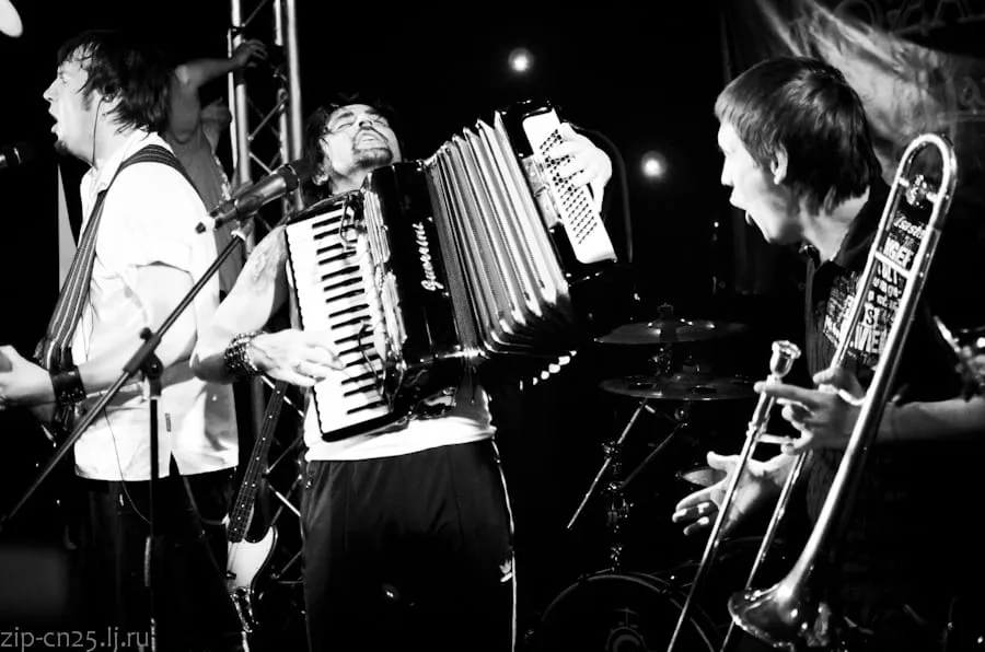 Czarno-białe zdjęcie z koncertu Kozak System: akordeonista i trębacz na scenie