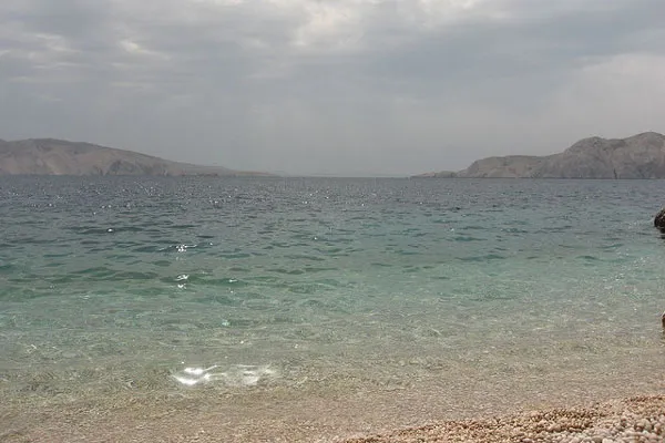 Żwirowy brzeg i spokojna woda w zatoce Baški