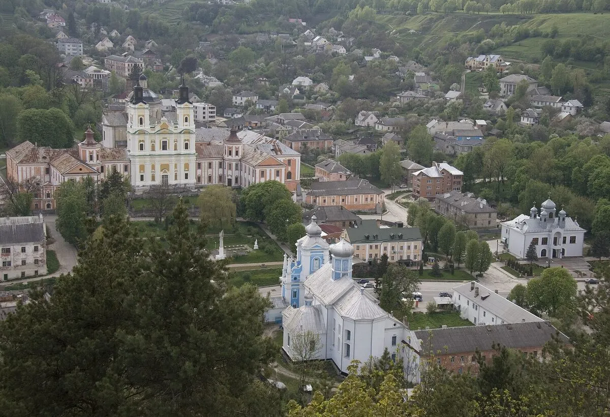 Widok z góry na Krzemieniec: barokowy kościół z dwiema wieżami, cerkiew i zabudowa miasteczka wśród zieleni