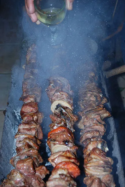 Polewanie winem mięsa pieczonego na rożnach nad węglem drzewnym
