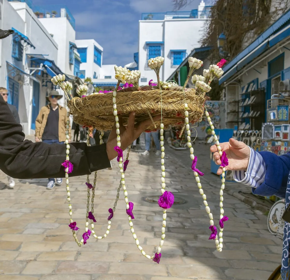 Sprzedawca trzyma koszyk z bukiecikami machmoum z pąków jaśminu i jaśminowymi naszyjnikami na uliczce Sidi Bou Saidu