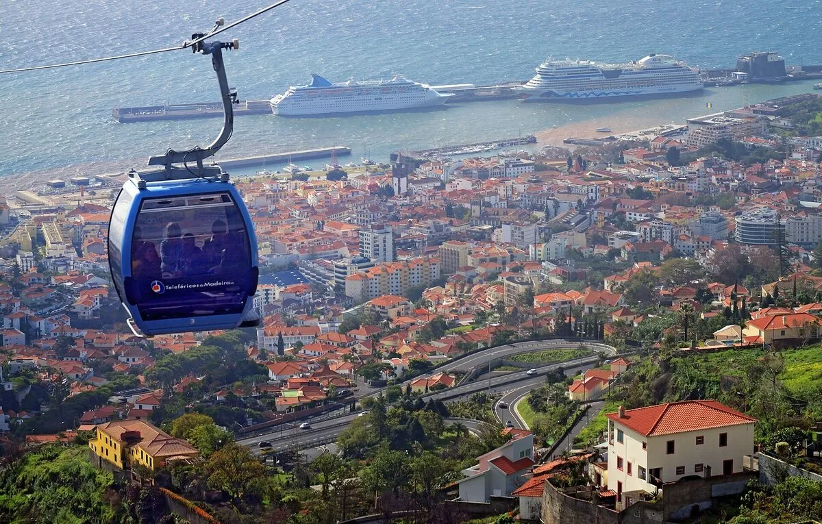 Niebieska gondola kolejki linowej nad dachami Funchal, w tle port z dwoma statkami wycieczkowymi