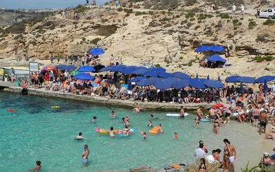 Tłum plażowiczów i niebieskie parasole nad Błękitną Laguną na Comino