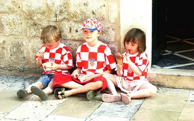 Troje dzieci w kibicowskich koszulkach w szachownicę jedzą lody na schodach