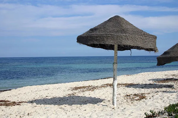 Słomiany parasol na piaszczystej plaży nad morzem w Marsa al-Kantawi