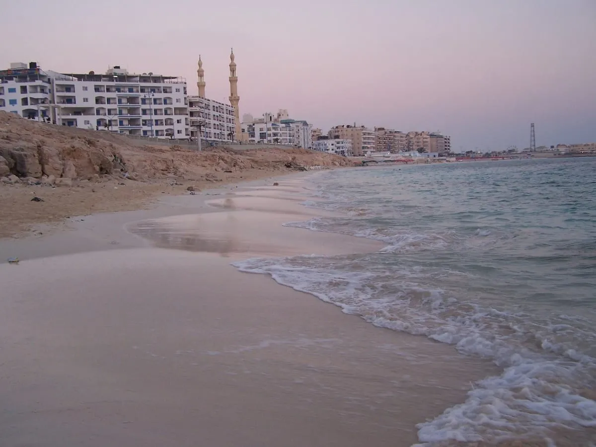 Piaszczysta plaża w Marsa Matruh o zmierzchu, za nią hotele i minarety meczetu
