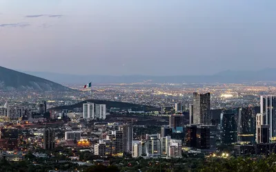 Panorama Monterrey o zmierzchu z wieżowcami, flagą Meksyku i górami w tle