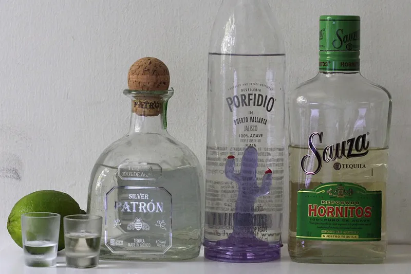Trzy butelki tequili, dwa kieliszki i limonka na białym stole