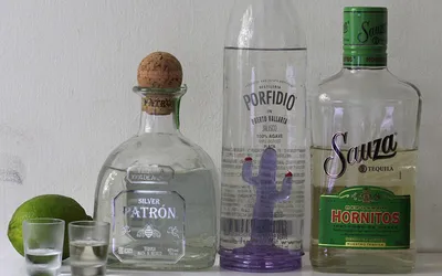 Trzy butelki tequili, dwa kieliszki i limonka na białym stole
