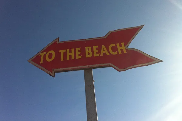 Czerwony drogowskaz z napisem „To the beach” na tle nieba