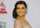 Uśmiechnięta Nelly Furtado w beżowej sukni na tle ścianki z logo Latin Grammy