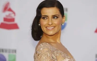 Uśmiechnięta Nelly Furtado w beżowej sukni na tle ścianki z logo Latin Grammy