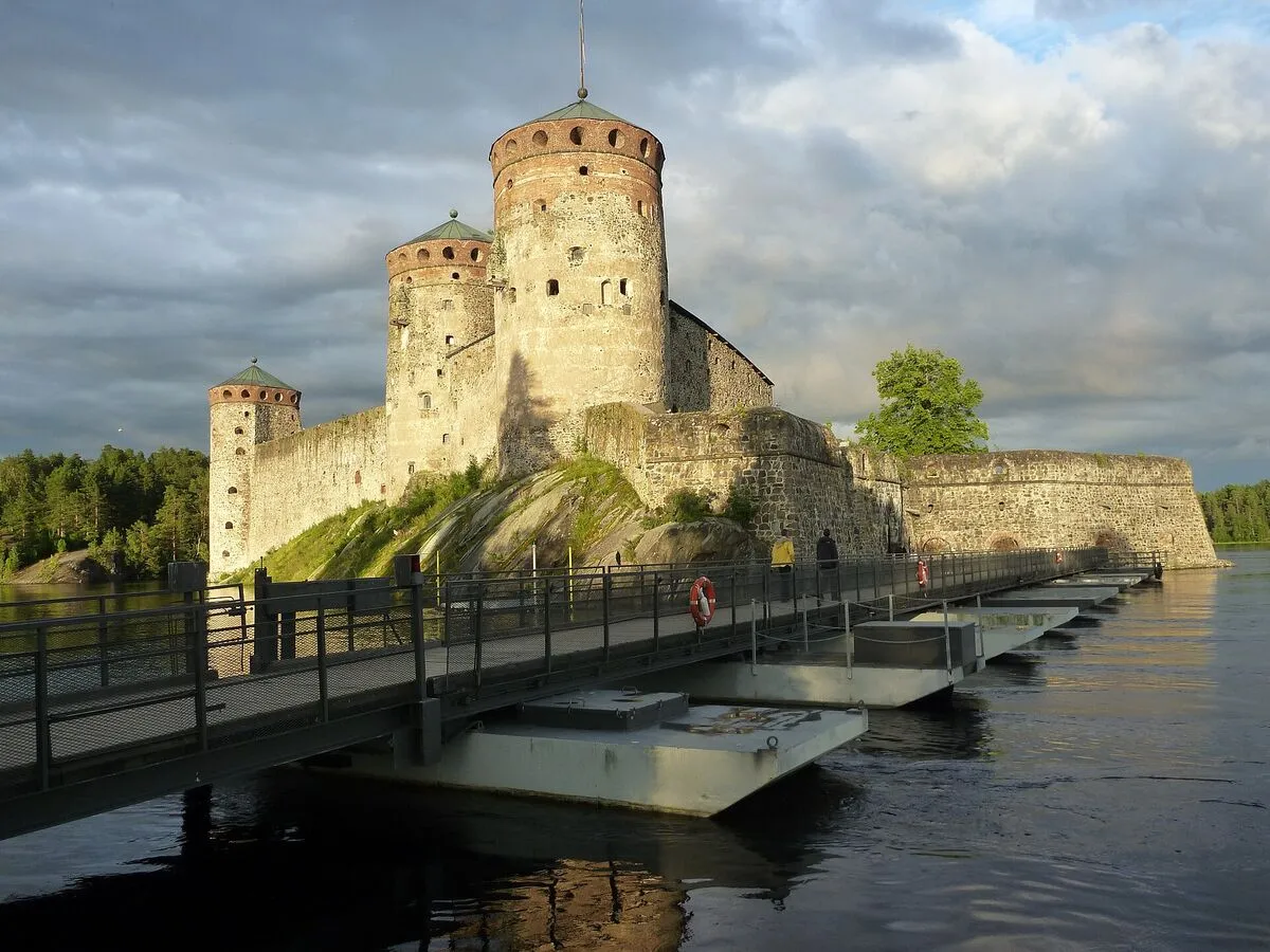 Zamek Olavinlinna na skale nad wodą, na pierwszym planie pływający most dla pieszych