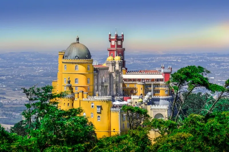 Żółte i czerwone mury Pałacu Pena z kopułą i wieżą zegarową ponad lasem Serra de Sintra